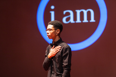 boy on stage with his hand on his heart in front of a "I am" backdrop