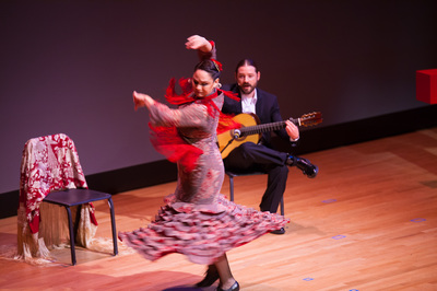 A woman dancing on stage while a man is sitting behind her playing his guitar
