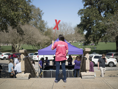 a volunteer standing in front of the student union holding a red x