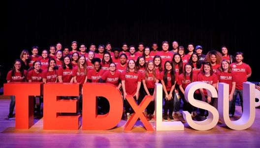 The student krewe on stage posing behind the TEDxLSU letters